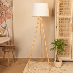 a floor lamp next to a potted plant in front of a wall with a painting on it