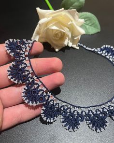 a hand holding a blue and white beaded necklace next to a rose on a table