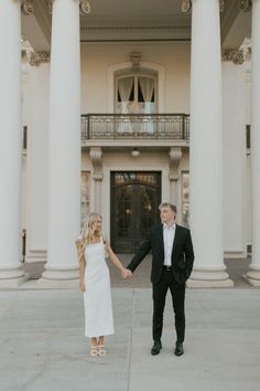 a man and woman holding hands in front of a large building with columns on both sides