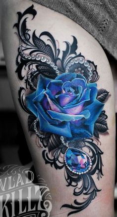 a blue rose tattoo on the side of a woman's thigh, with an ornate design