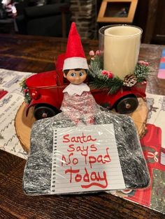 an elf sitting on top of a piece of paper next to a candle and christmas tree