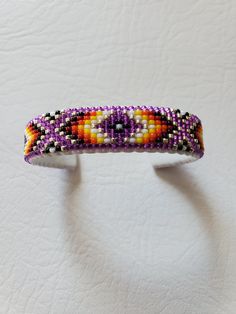 a beaded bracelet is displayed on a white surface with an orange, yellow and purple pattern