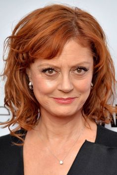 a woman with red hair wearing a black dress and diamond necklace smiling at the camera