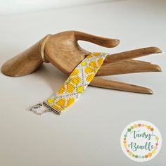 a wooden hand holding a yellow and white bracelet