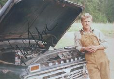 a man standing next to an old car with the hood open and his hand on it