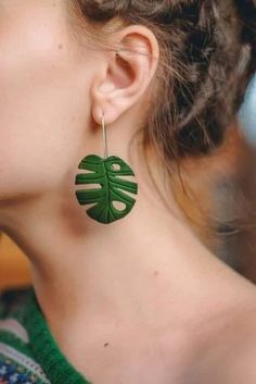 a close up of a person wearing large earrings with green leaves on the back of them