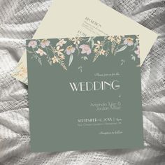 two wedding cards with flowers on them sitting on top of a white cloth covered bed