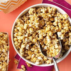 a bowl filled with popcorn sitting on top of a table next to two spoons