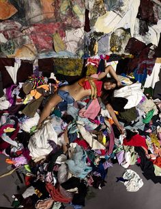 a woman laying on top of a pile of clothes next to a wall covered in cloths