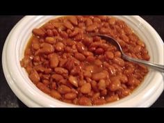 a white bowl filled with baked beans on top of a black countertop next to a silver spoon