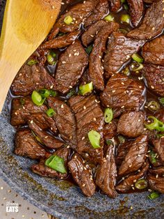 beef and sesame seed stir fry in a bowl with a wooden spoon on the side