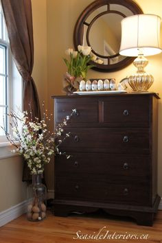 a dresser with vases and flowers on it next to a mirror