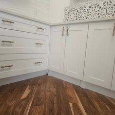 a kitchen with white cabinets and wood flooring in the middle of an empty room