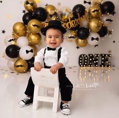 a little boy sitting on a chair in front of some balloons and gold foil decorations