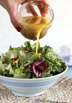 someone pouring dressing into a salad in a bowl