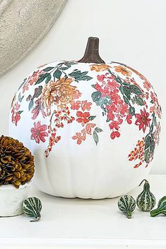 a white painted pumpkin sitting on top of a table next to some pine cones and other decorations