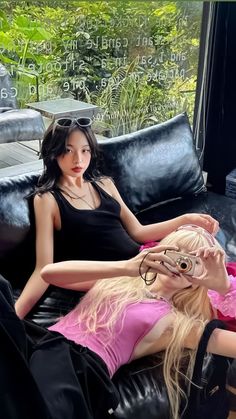 two beautiful young women sitting on top of a black leather couch next to each other