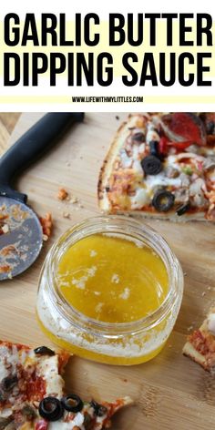 garlic butter dipping sauce in a glass jar next to sliced pizza on a cutting board