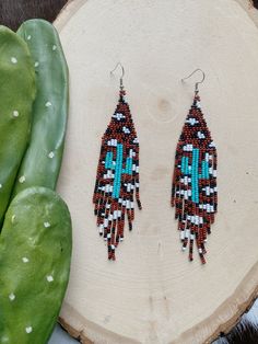 a pair of beaded earrings sitting on top of a piece of wood next to a cactus