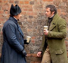 two men standing next to each other with cups in their hands and one holding a coffee cup