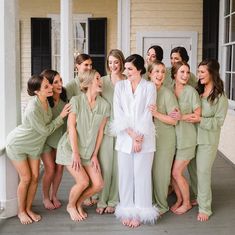 a group of women standing next to each other in front of a white house wearing green robes