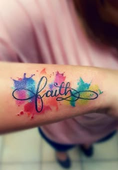 a person with a tattoo on their arm that says faith in watercolor paint splatters