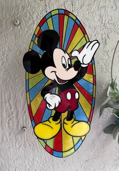 a stained glass mickey mouse hanging on the wall next to a potted green plant