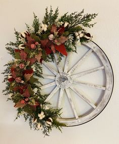 a wreath with red and white flowers is hanging on the wall next to a wagon wheel