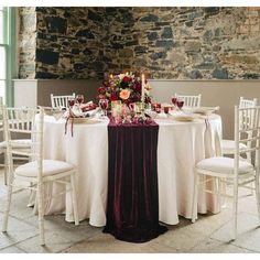 the table is set with white linens and red flowers, along with other chairs