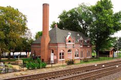 an old brick train station sits on the tracks next to a grassy area with trees