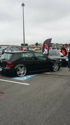 there are many cars that are parked in the parking lot with people standing around them