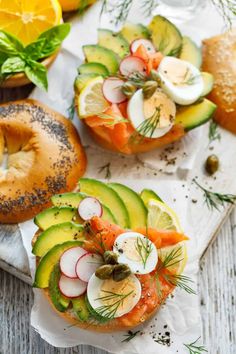 two bagels topped with salmon, cucumber and radishes on top of each other