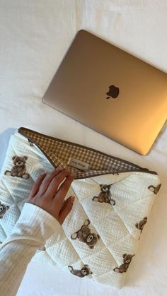 an apple laptop computer sitting on top of a white bed next to a woman's hand