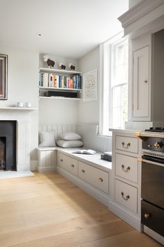 a kitchen with white cabinets and an oven in front of a window that has books on the shelves