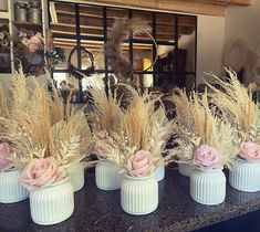 four white vases filled with dried flowers on top of a black counter in front of a mirror