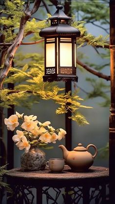 a tea pot with flowers on a table next to a lamp and some rocks in front of it