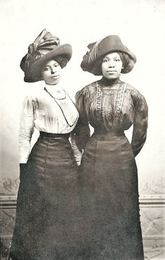 two women standing next to each other with hats on their heads and one wearing a dress