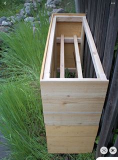 a wooden box sitting in the grass next to a fence and some tall green plants