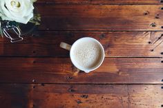 a cup of coffee sitting on top of a wooden table next to a vase with flowers