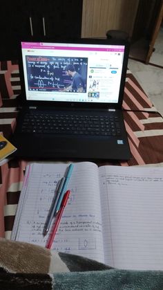 a laptop computer sitting on top of a bed next to an open notebook and pen