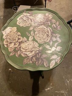 a green table with flowers painted on the top is sitting next to a black chair