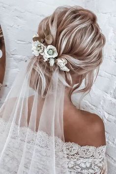 a woman with blonde hair wearing a veil and flowers in her hair is looking into the mirror