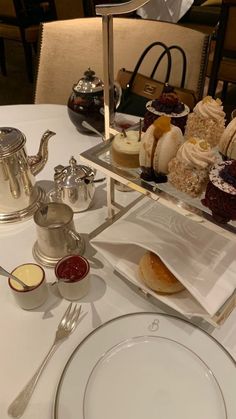 a table topped with plates and cups filled with desserts next to silver teapots