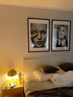 a bed with two pictures on the wall above it and a white cat laying on top