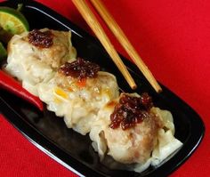 some food on a black plate with chopsticks next to it and a red table cloth