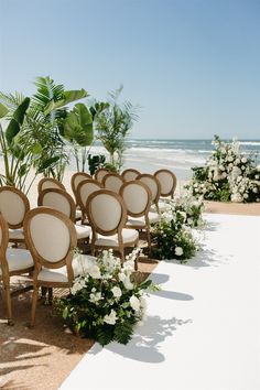 rows of chairs set up on the beach for an outdoor ceremony with flowers and greenery