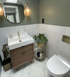 a white toilet sitting next to a sink in a bathroom under a large round mirror