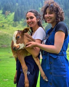 two girls are holding a baby cow in their arms