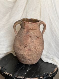 a brown vase sitting on top of a wooden table next to a white wall and black stool