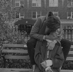 two people are sitting on a bench in front of a building and one is hugging the other